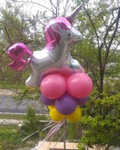 Unicorn foil balloon on top of round pink, purple, and yellow balloons for outside decoration 