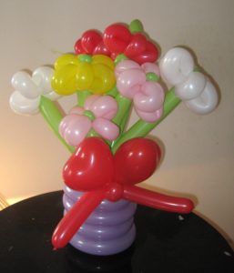 Colorful balloon flowers in a purple balloon vase with a red bow - decor and deliveries