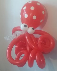 Octopus balloon for a child's party. The head is a round red balloon with polka dots. The eight tentacles are also red. The eyes are made out of small round white balloons  