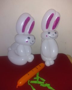 Two small white balloon rabbit with pink ears and a balloon carrot twisted for kids' parties