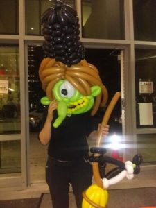Witch balloon mask with a green face and a tall black balloon hat with a balloon broom with a black balloon cat attached for a Halloween event